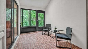 A balcony with a tiled floor, two chairs, a small table, and a window with a view of greenery. - Sea Woods Villa 4263 (New Smyrna Beach)