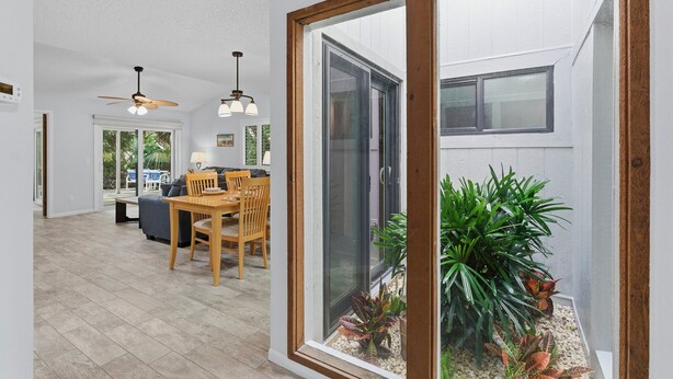 Un intérieur moderne comprenant un coin repas, un ventilateur de plafond et une vue sur un jardin, accessible par une porte vitrée.
