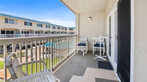 A balcony with white chairs, a pool, and a building with multiple windows in the background. - Win-san C214 (New Smyrna Beach)