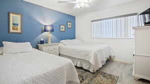 A bedroom with two beds, a nightstand, a lamp, a dresser, and a window with blinds. - Win-san C214 (New Smyrna Beach)