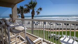 A balcony with white chairs and tables, overlooking a beach with palm trees and the ocean. - Win-san C214 (New Smyrna Beach)