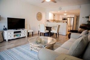 A modern living room with a flat-screen TV, a glass coffee table, a sofa, and a dining area with chairs. - Win-san C213 (New Smyrna Beach)
