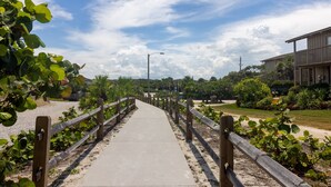 A concrete pathway flanked by wooden railings, leading to a building with a balcony. - Sea Woods Condo 169 (New Smyrna Beach)