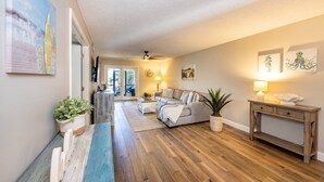 A living room with a sofa, coffee table, and console table. There is a plant on the console table and a plant on the coffee table. - Sea Woods Condo 169 (New Smyrna Beach)