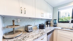 A kitchen with white cabinets, a granite countertop, a toaster, a slow cooker, and a coffee maker. - Sea Woods Condo 169 (New Smyrna Beach)