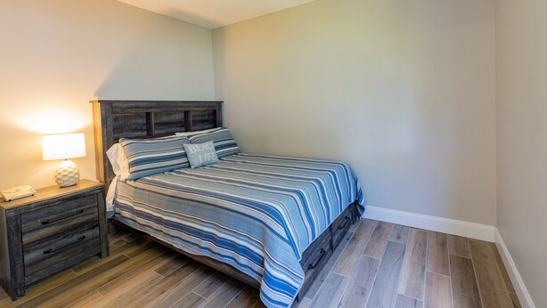A bedroom with a bed, nightstand, and lamp. - Sea Woods Condo 169 (New Smyrna Beach)