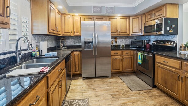 A modern kitchen with wooden cabinets, stainless steel appliances, and a granite countertop. - Win-san A101 (New Smyrna Beach)
