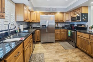 A modern kitchen with wooden cabinets, stainless steel appliances, and a granite countertop. - Win-san A101 (New Smyrna Beach)
