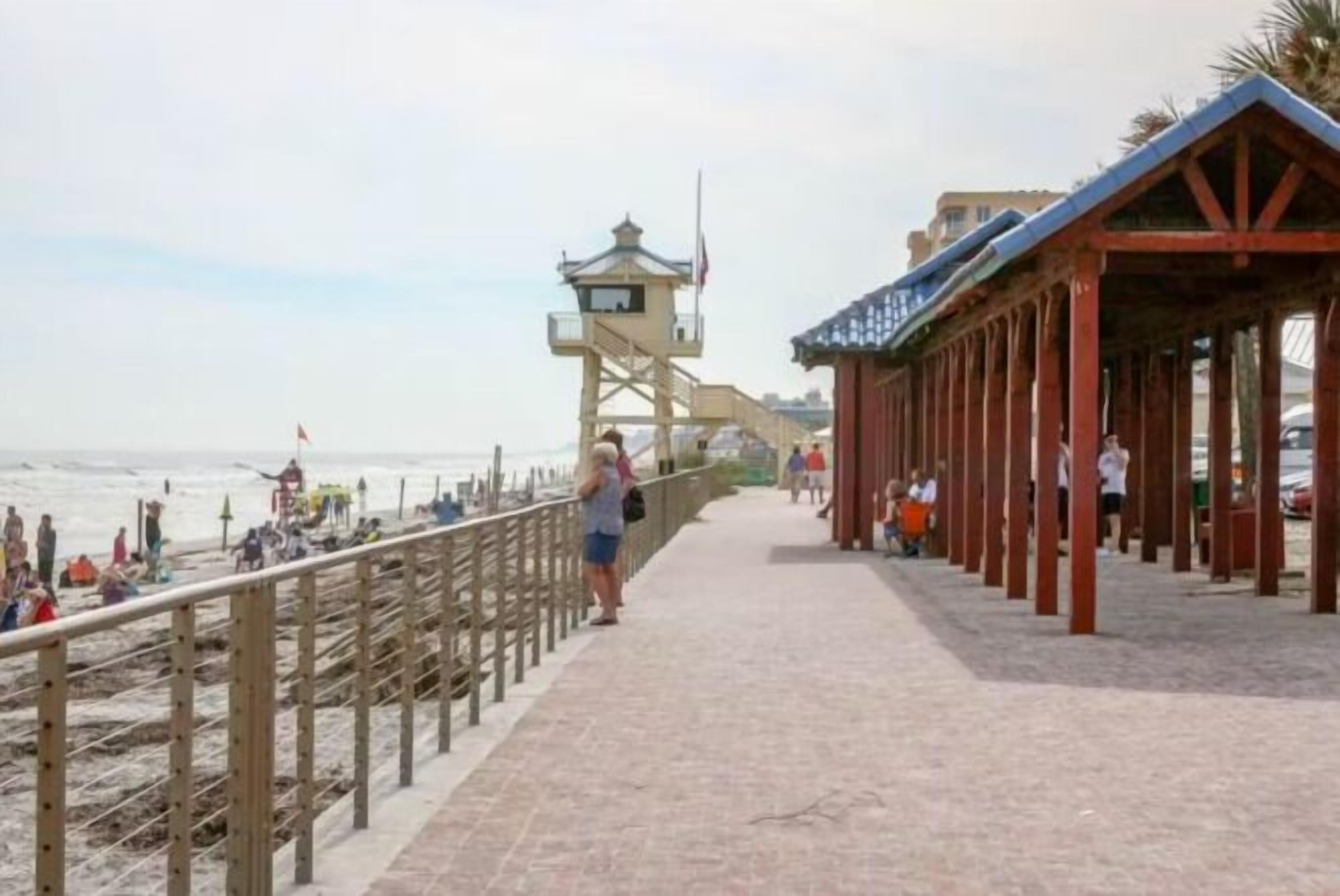 En strandpromenad med ett räddningstorn, träräcken och ett överbyggt sittområde.