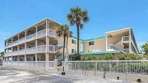 A multi-story hotel with balconies, a palm tree, and a clear blue sky. - Win-san A101 (New Smyrna Beach)