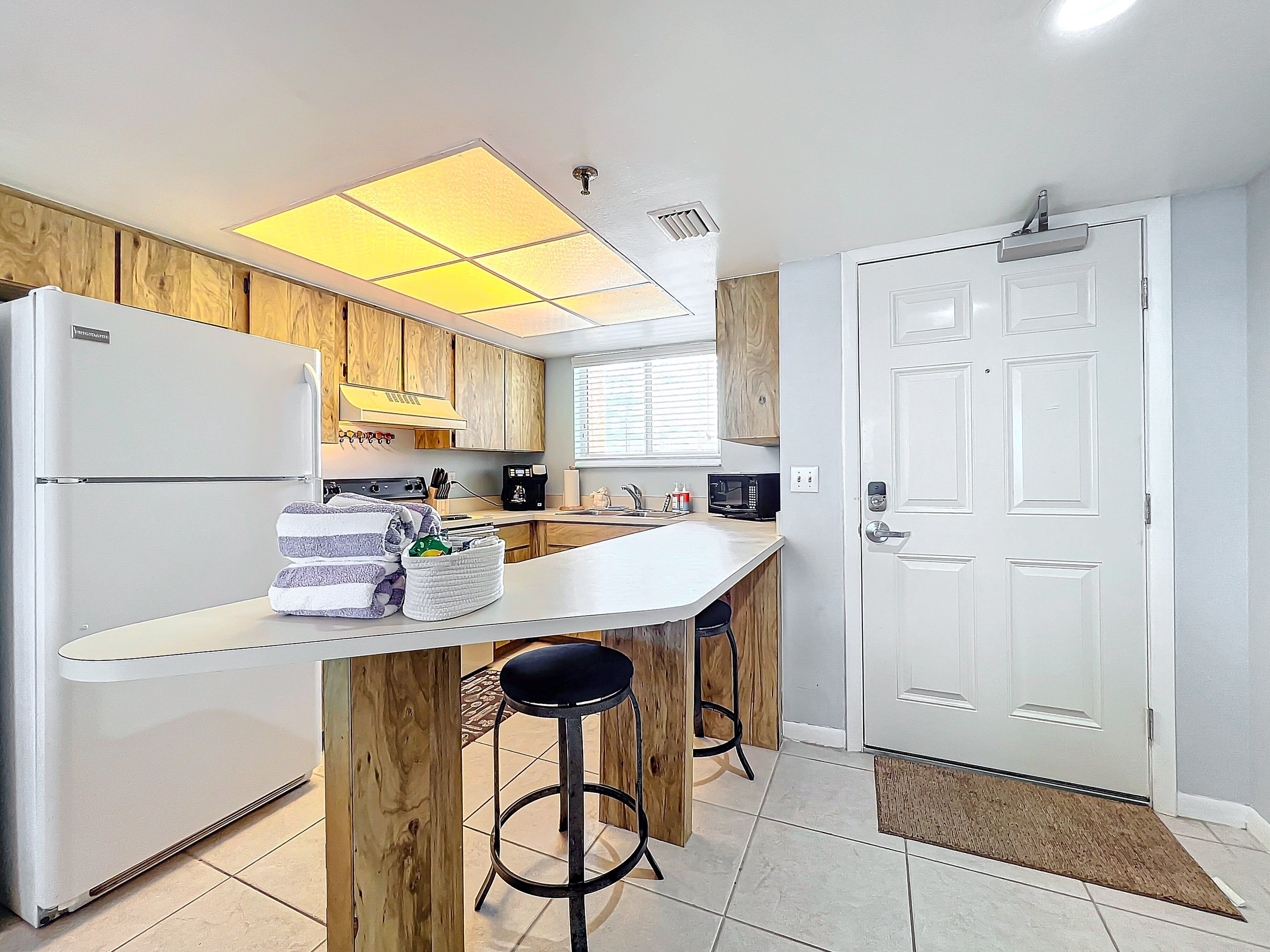 Una cocina moderna con un refrigerador blanco, armarios de madera, un taburete de bar y una puerta blanca.