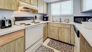Une cuisine compacte avec des meubles en bois, une cuisinière blanche, un grille-pain, une machine à café et un four à micro-ondes.