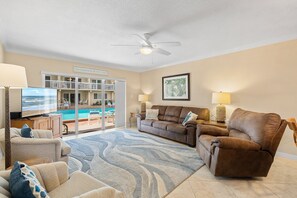 Ein Wohnzimmer mit einer Couch, Sesseln, einem Fernseher und Blick auf einen Pool.