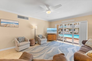 Ein Wohnzimmer mit Blick auf Pool und Balkon, mit beige gestrichenen Wänden und Deckenventilator.