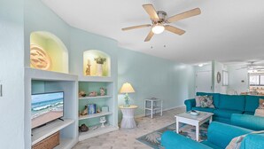 Un soggiorno con televisione, divano color petrolio e ventilatore a soffitto.