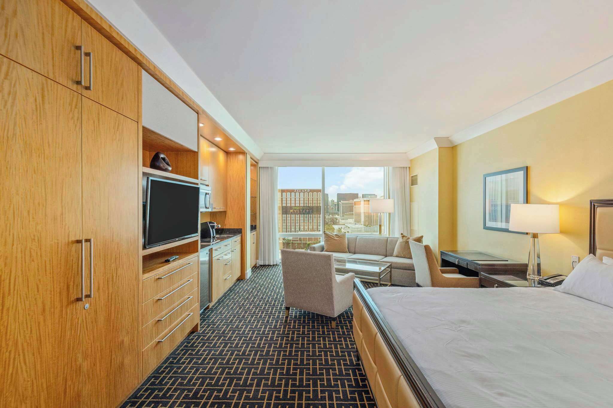 Ein Hotelzimmer mit Bett, Fernseher, Schreibtisch, Stuhl und Blick auf die Stadt.