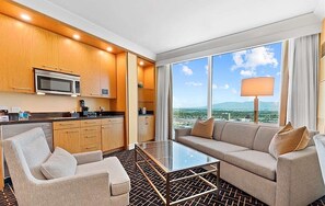 Ein modernes Hotelzimmer mit Küchenbereich, einer Couch, einem Couchtisch und einem großen Fenster mit Blick auf die Stadt.