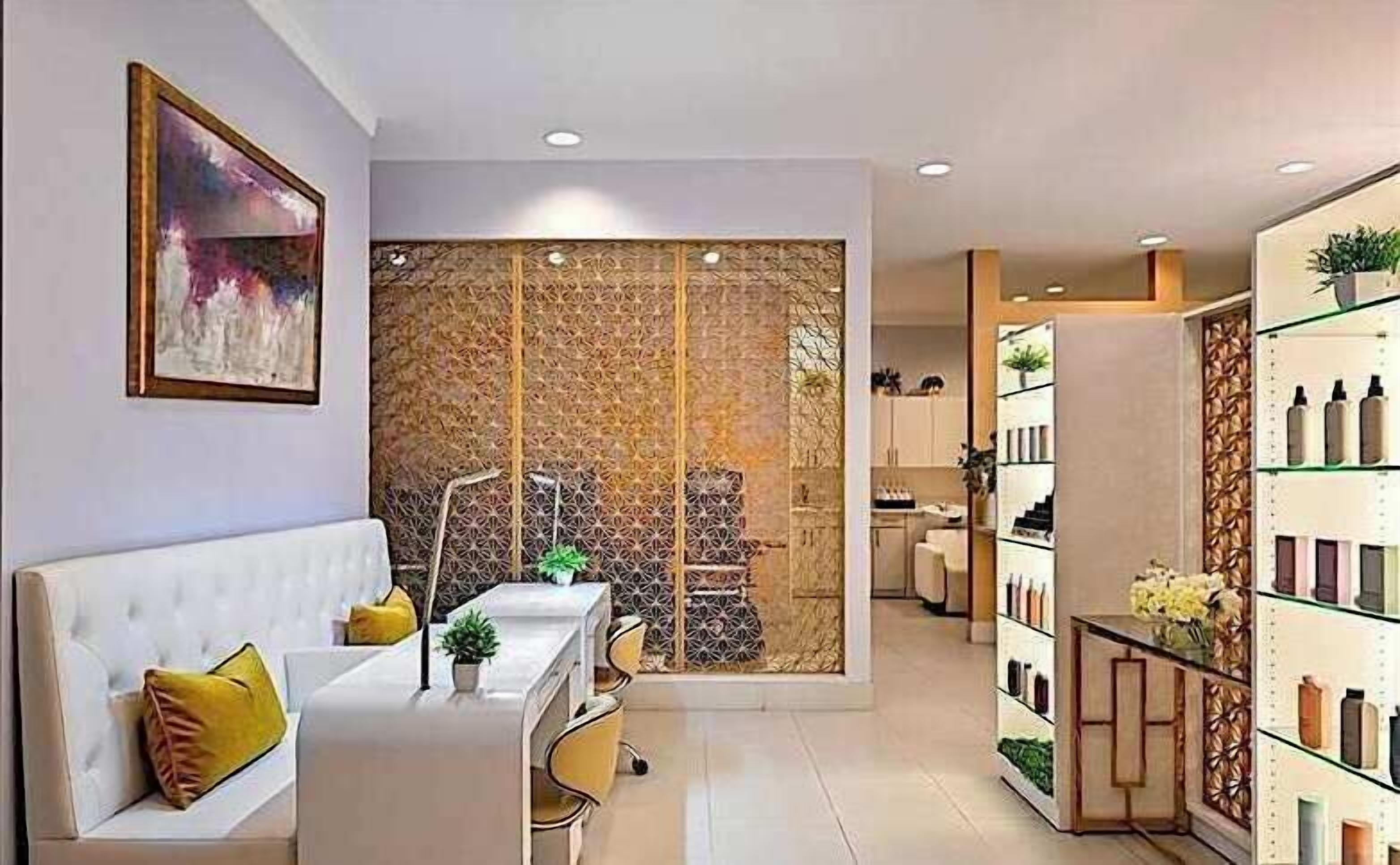 A modern living room with a white sofa, a small table, and a decorative screen. There is a kitchen area with cabinets and a refrigerator.