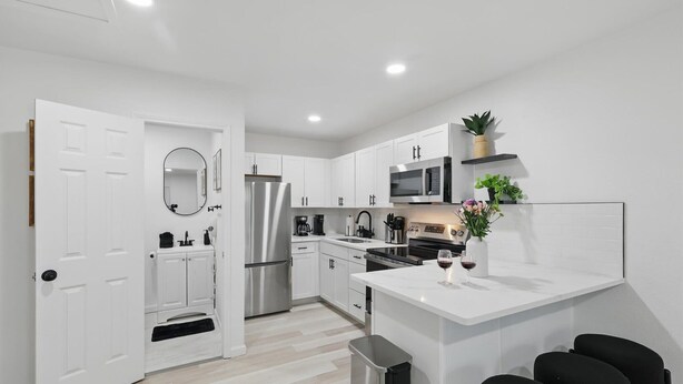 A modern kitchen with white cabinetry, stainless steel appliances, and a white island with bar stools. - Modern 4BR 2BA Home With Hot Tub-grill & Huge Yard (Haltom City)