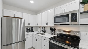 A modern kitchen with white cabinets, a stainless steel refrigerator, a microwave, and an oven. - Modern 4BR 2BA Home With Hot Tub-grill & Huge Yard (Haltom City)