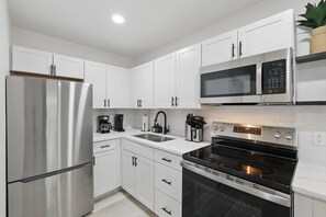 A modern kitchen with white cabinets, a stainless steel refrigerator, a microwave, and an oven. - Modern 4BR 2BA Home With Hot Tub-grill & Huge Yard (Haltom City)