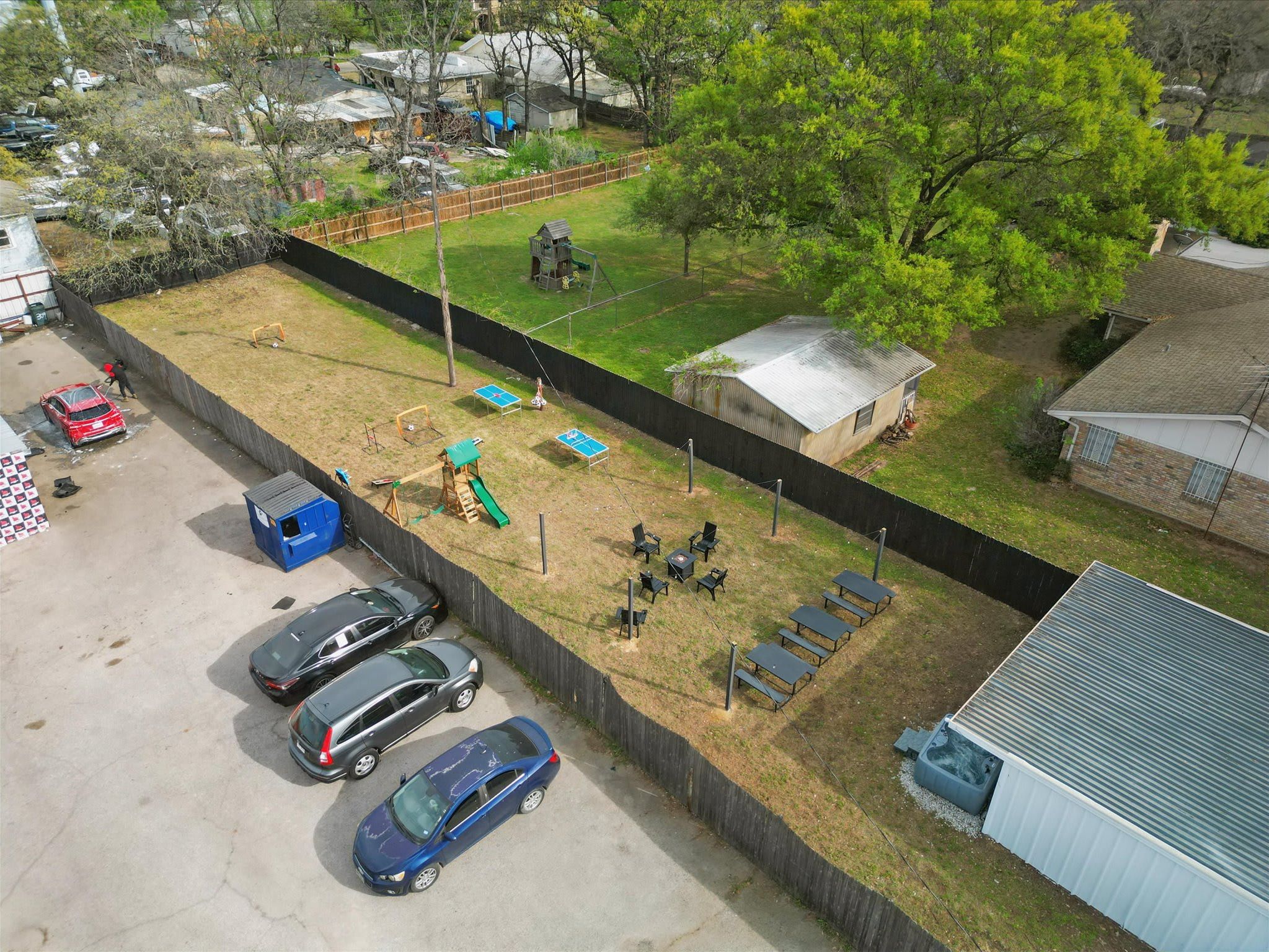An aerial view of a fenced backyard with a playground, a small shed, and a carport with parked cars.