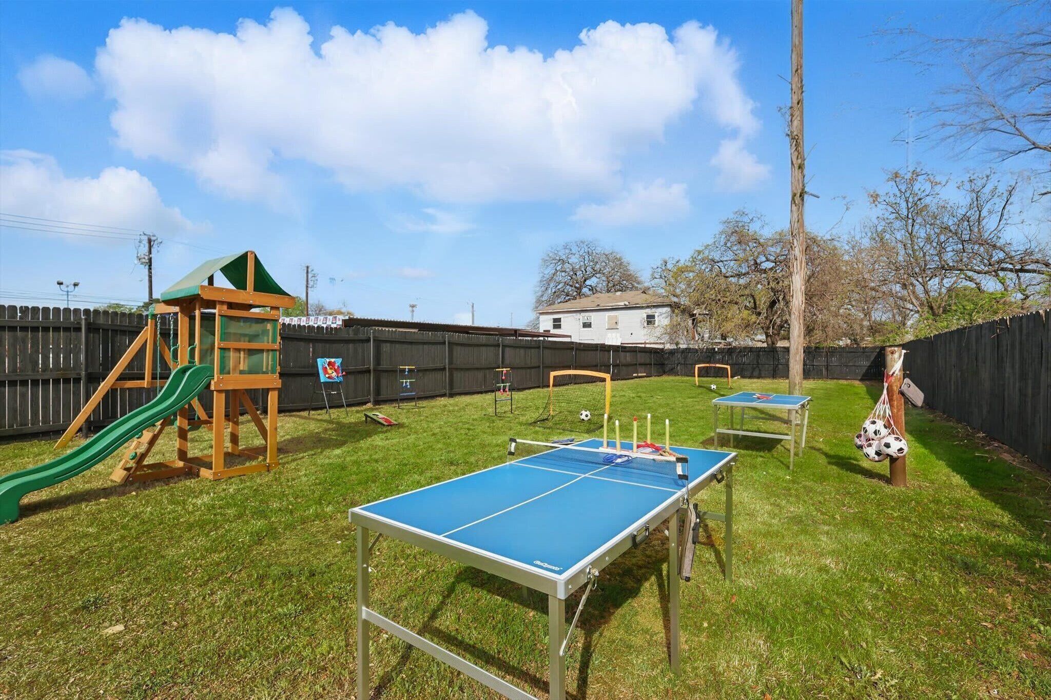 Un patio trasero con mesa de ping pong, un tobogán y una casita de juegos.