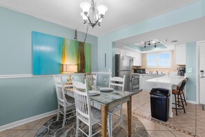 A modern kitchen with a dining area, featuring a large island, white cabinetry, and a colorful abstract painting on the wall. - Oceania Beach Club 803 (New Smyrna Beach)