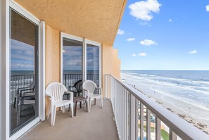 A balcony with a view of the ocean, equipped with plastic chairs and a table. - Oceania Beach Club 803 (New Smyrna Beach)
