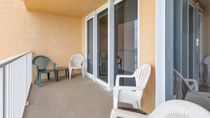 A balcony with sliding glass doors, two white plastic chairs, and a green plastic chair. - Oceania Beach Club 803 (New Smyrna Beach)