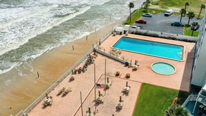 Ein Luftbild eines Hotels direkt am Strand mit Swimmingpool, Sitzgelegenheiten am Strand und einem Parkplatz.