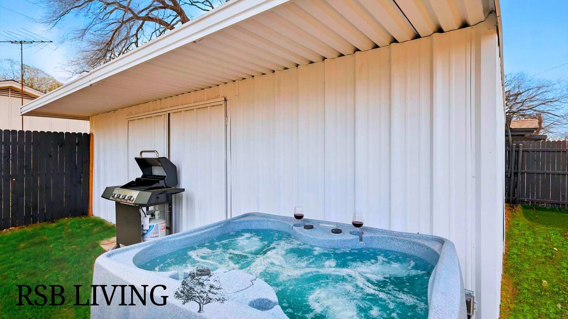 A backyard with a hot tub, a grill, and a fenced area.