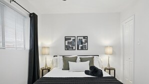 Un dormitorio ordenado con cama, dos lámparas de noche, una ventana con persianas y una puerta.