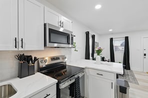 A modern kitchen with white cabinets, a stainless steel sink, a black stove, and a microwave. - Modern 2BR Unit Hot Tub Outdoor Lounge (Haltom City)