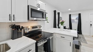 Una cocina moderna con armarios blancos, un lavamanos de acero inoxidable, una estufa negra y un microondas.
