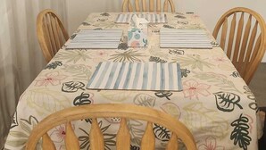 En matplats med ett bord dukat för fyra personer, med ett blommigt bordsduk, randiga underlägg och trästolar.