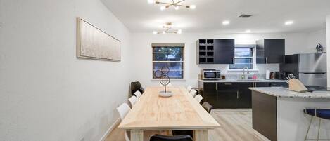 Una cocina moderna con una isla central, electrodomésticos integrados y un comedor con una mesa grande.