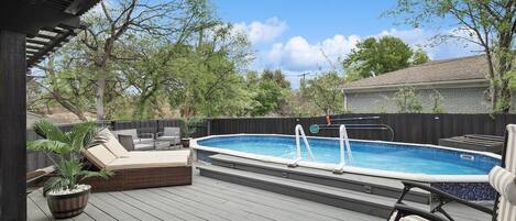 Un patio trasero con piscina, sillas de deck y un área de patio cubierta.