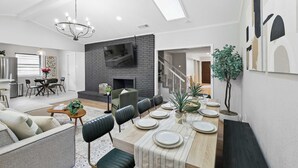 A modern living room with a fireplace, dining area, and a staircase leading to another level. - Spacious 5BR 3BA Retreat With Pool & Hot Tub (Duncanville)