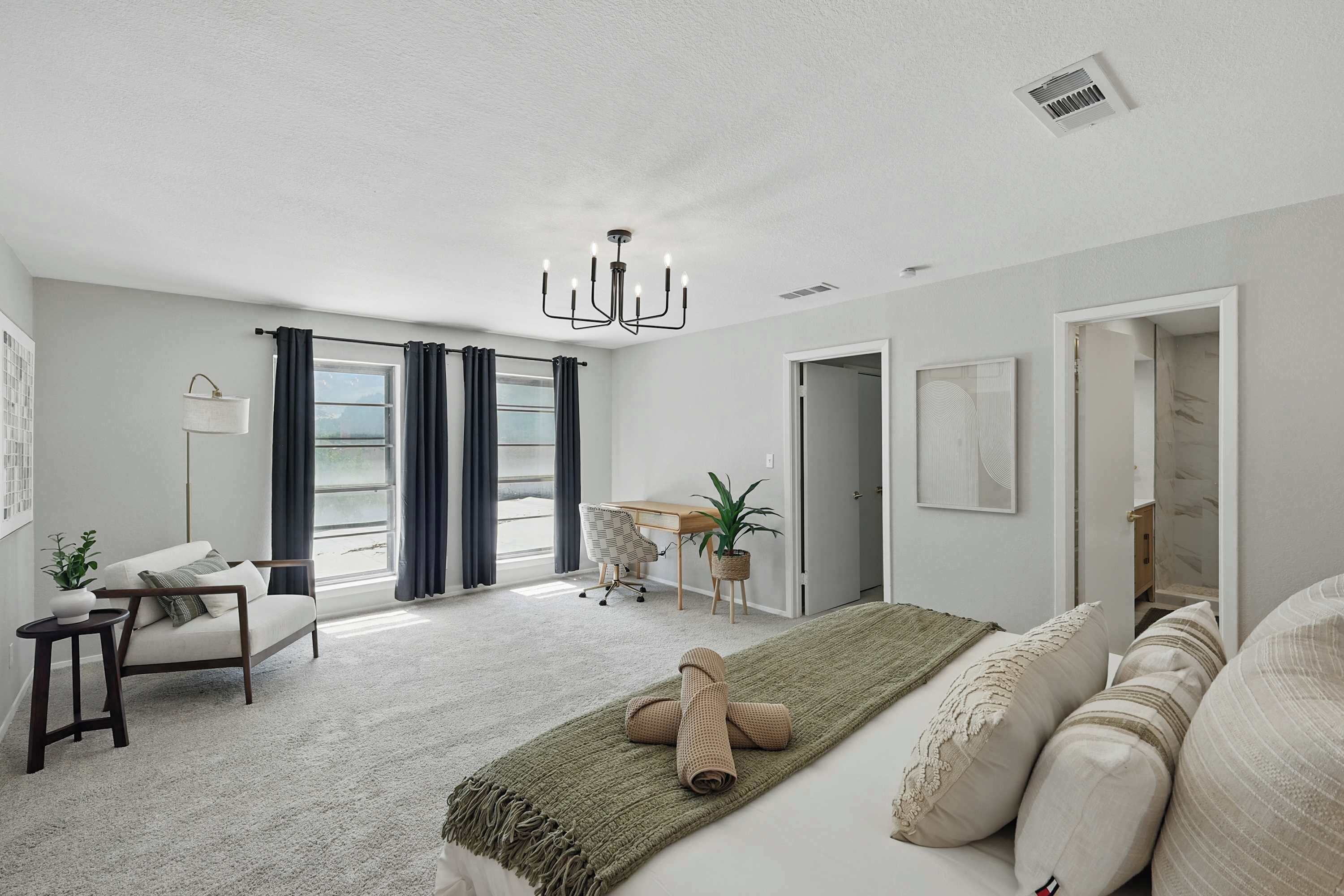 A modern bedroom with a large bed, a desk, and a chair, a window with curtains, and a chandelier.