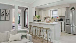 A modern kitchen with white cabinets, a stainless steel refrigerator, and a bar area with stools. - Spacious 5BR 3BA Retreat With Pool & Hot Tub (Duncanville)