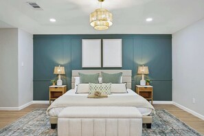 A bedroom with a bed, two bedside tables, a chandelier, and a large window. - Spacious 5BR 3BA Retreat With Pool & Hot Tub (Duncanville)