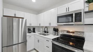 A modern kitchen with white cabinets, a stainless steel refrigerator, a microwave, a stovetop, and a coffee maker.