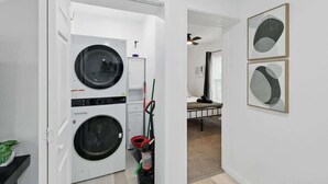 A laundry room with a washing machine, dryer, and ironing board. There are two framed abstract paintings on the wall. - Modern 2BR Unit With Hot Tub (Haltom City)