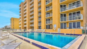 Une piscine avec des chaises longues et un bâtiment doté de nombreux balcons.