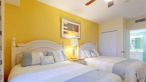Une chambre avec deux lits, une table de chevet avec une lampe et une porte donnant sur une salle de bain.