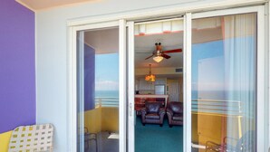 Une pièce dotée d’une porte-fenêtre coulissante donnant sur un balcon, d’un ventilateur de plafond et offrant une vue sur la cuisine.