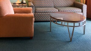 A room with a patterned sofa, a brown armchair, a small round table, two lamps, and a ceiling fan. - Ocean Walk 2424a (Daytona Beach)