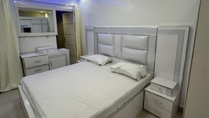 A modern bedroom with a central bed, bedside tables, a built-in wardrobe, and a ceiling light fixture. - DAKAR VDN: Furnished apartment for rent- 2 bedrooms- Living room - 3 bathrooms (Dakar)