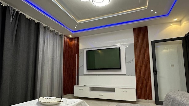 A modern living room with a flat-screen TV, grey sofa, and a small table with a white tablecloth. - DAKAR VDN: Furnished apartment for rent- 2 bedrooms- Living room - 3 bathrooms (Dakar)